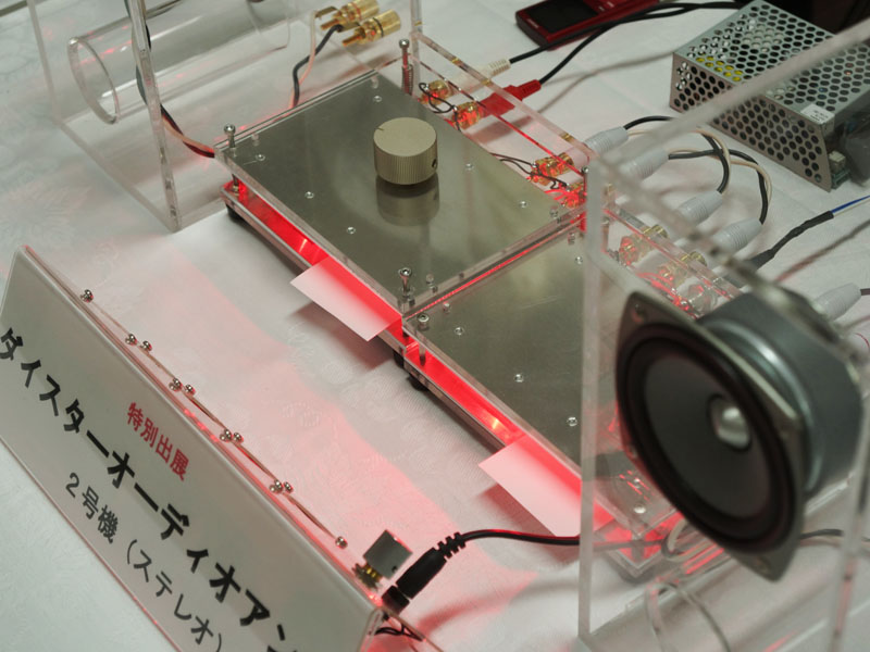 香川大学工学部のブースでは、世界初という“光アンプ”を展示。通常のアンプはトランジスタやIC、真空管などの増幅素子が使われるが、発光ダイオード(LED)とフォトダイオード(光センサー)から作られた増幅素子「ダイスター(distar)を発明・採用しているのが特徴。岡本研正教授の発明で、原理としては、LEDの光をフォトダイオードで受け、太陽電池のように発電。その電気を戻してLEDの発光をさらに強くし、その光で発電……というサイクルを繰り返して増幅するという。ブースでは光を遮ると音が出なくなるなど、試作アンプから実際に音を出して原理を説明している